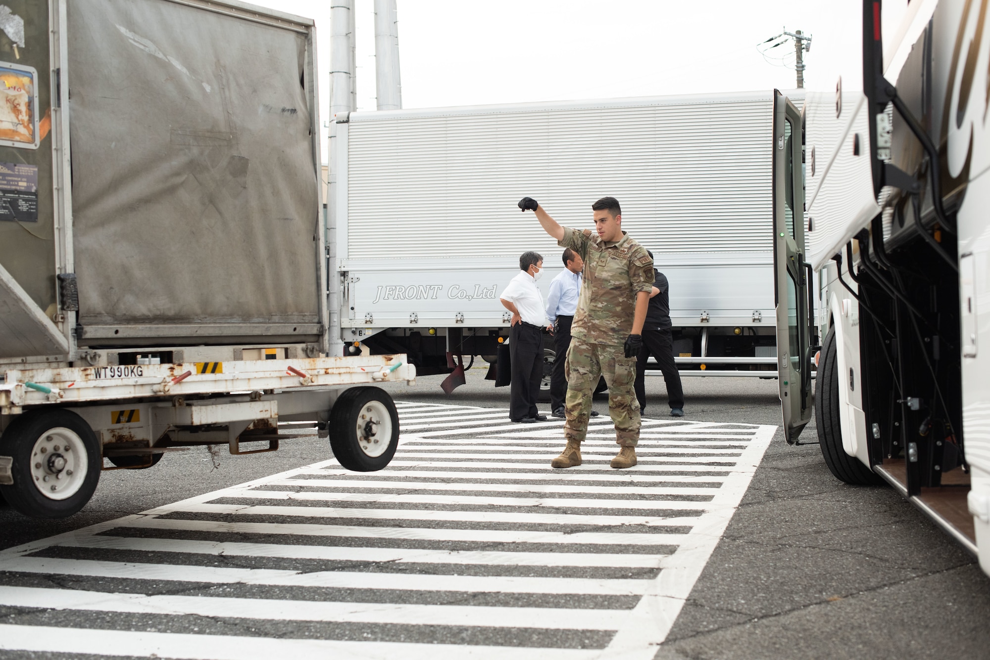 A U.S. Air Force Airman guides a forklift holding a container towards a bus with the undercarriage ajar.