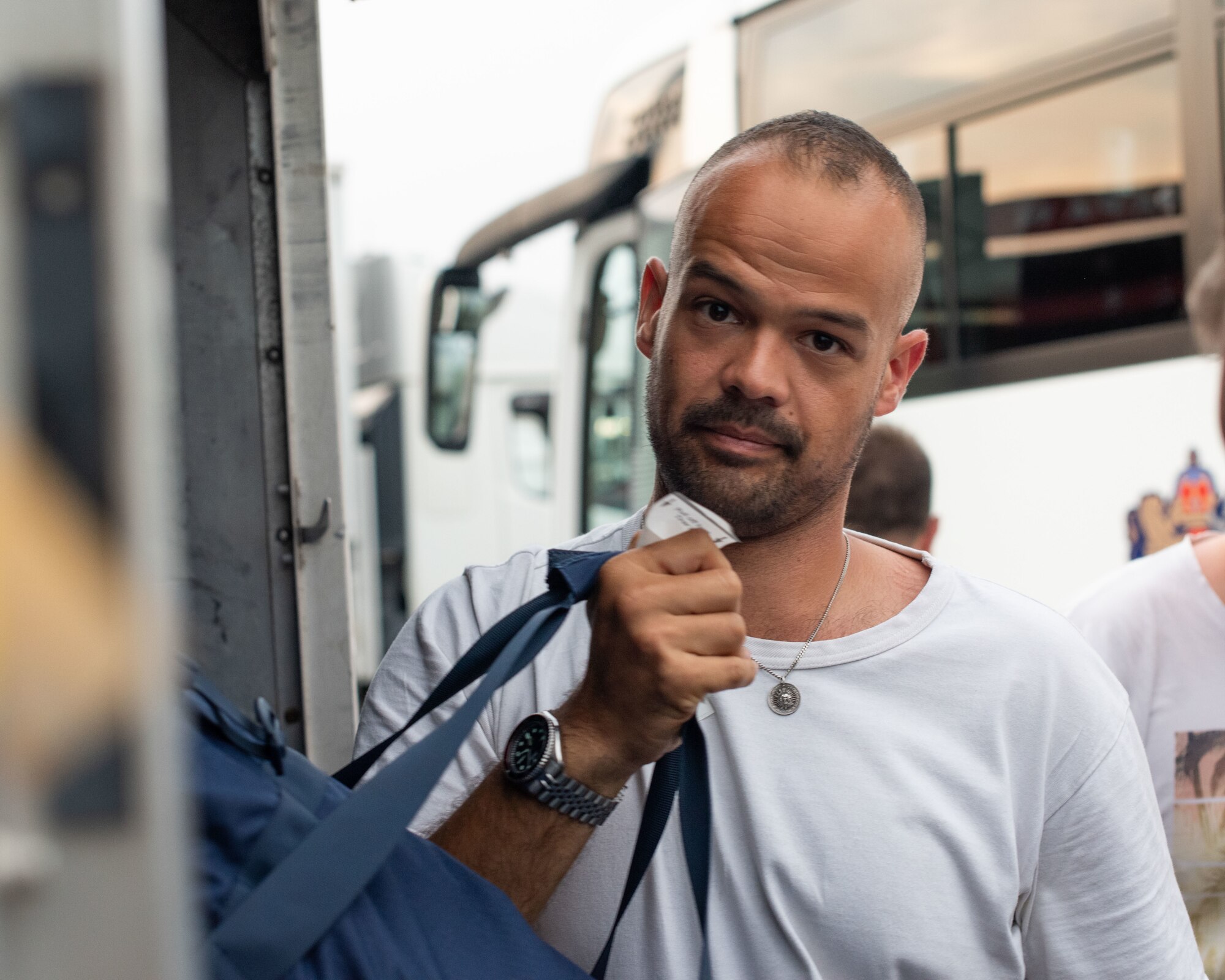 A man stares into the camera while holding luggage in his right hand.