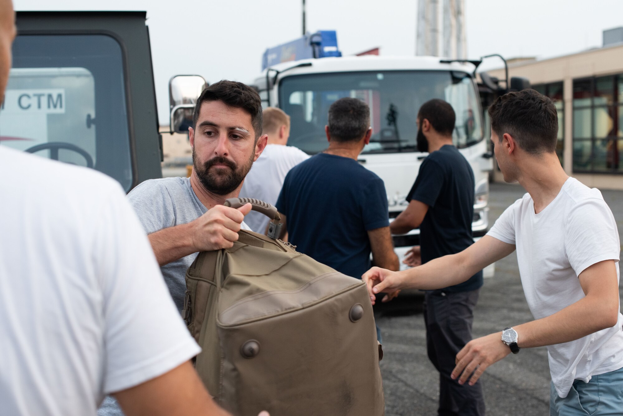 Men carry a bag from a truck through a line towards the camera.