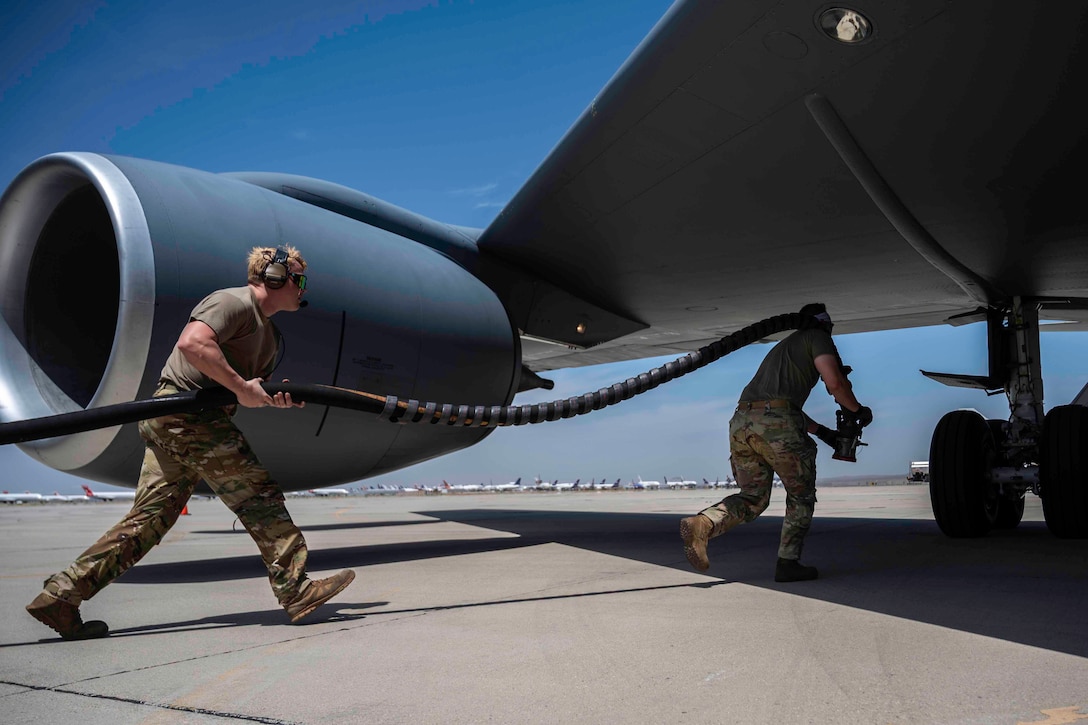 Two airmen carry a long fuel hose as they move quickly to the underside of an aircraft.