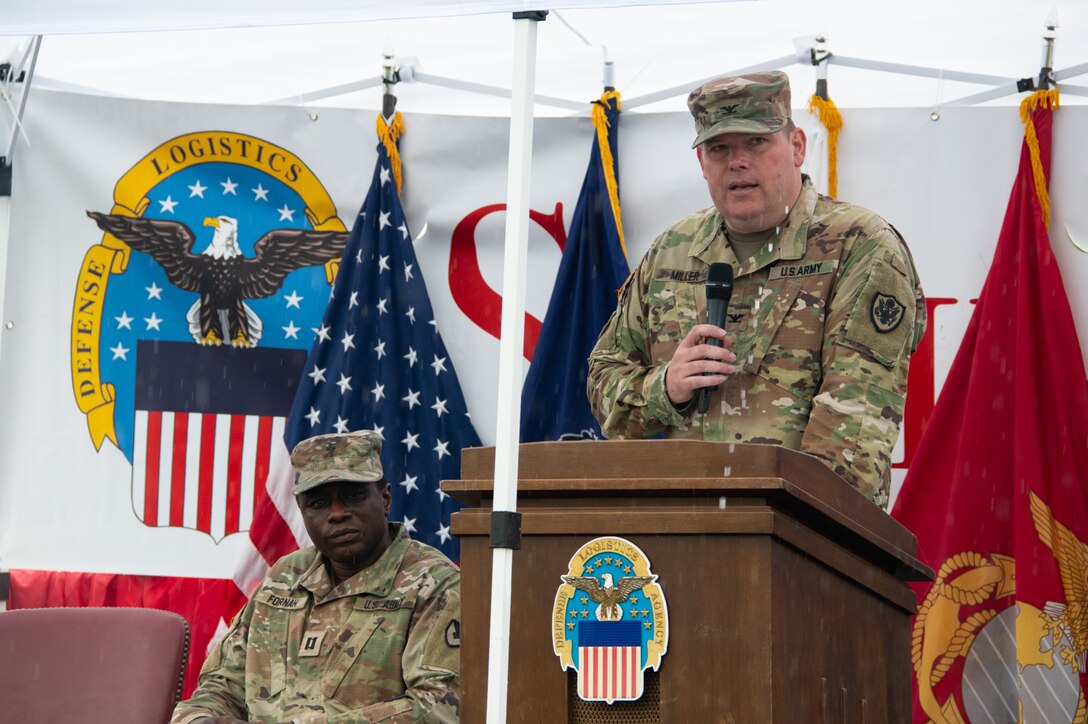 An Army officer in camouflage speaks into a microphone at a podium.