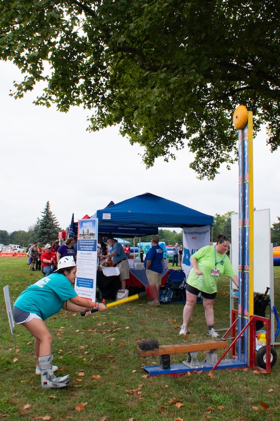 A girl swings a hammer to play a high striker carnival game.
