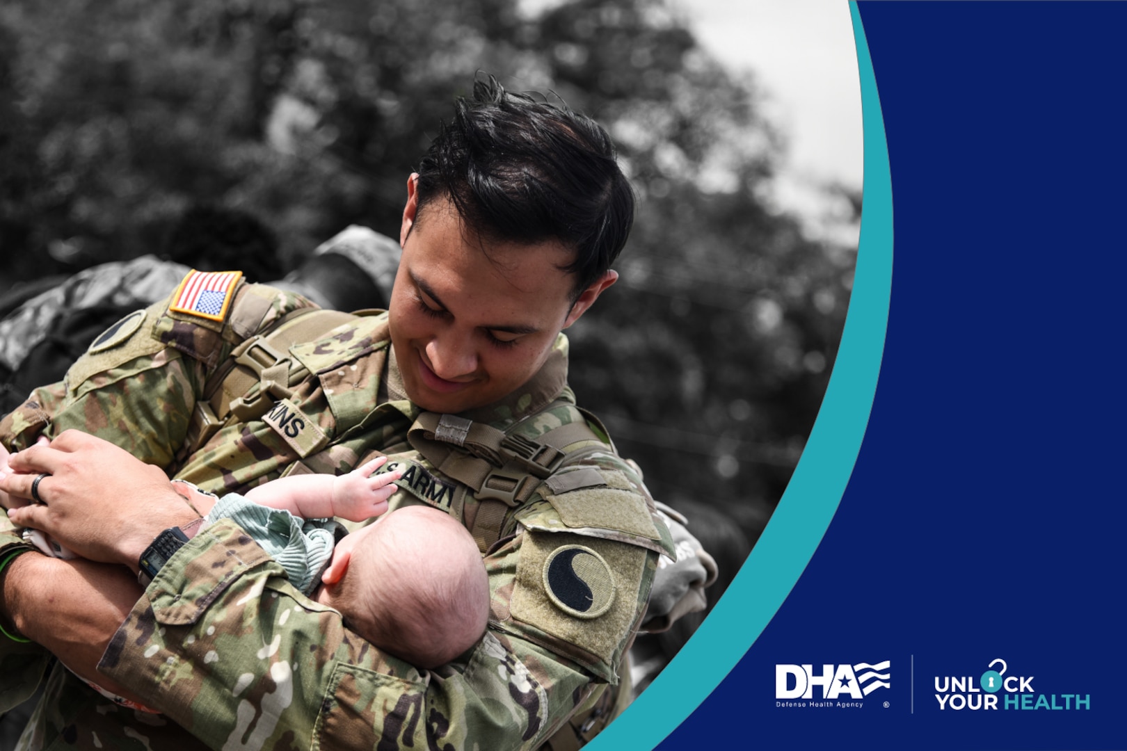 Uniformed service member stands outside and holds infant in his arms.