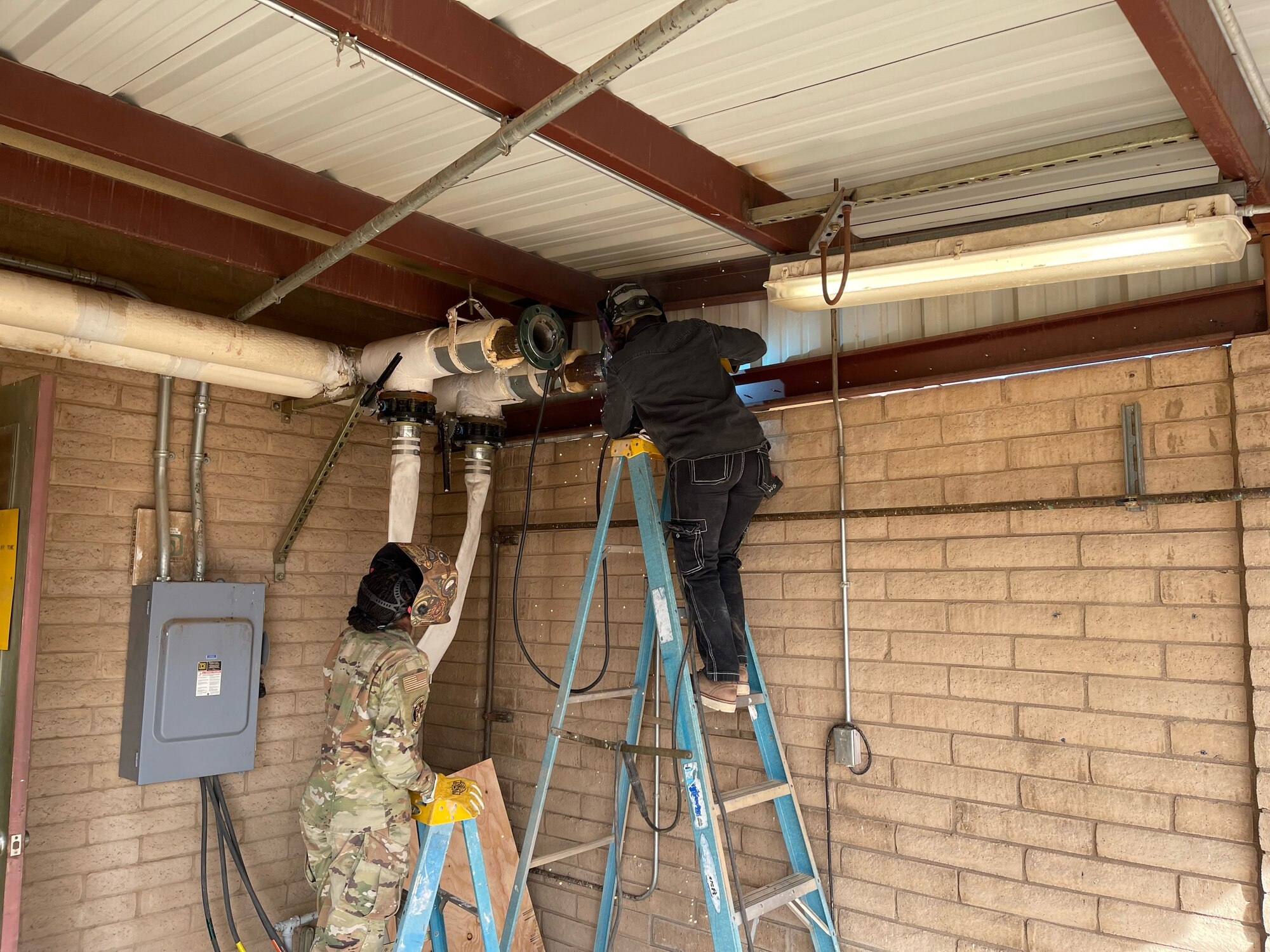 A U.S. Air Force Airman and government civilian assigned to the 56th Civil Engineer Squadron weld together new piping during a renovation of the base gym and chapel heating, ventilation, and air conditioning systems, at Luke Air Force Base, Arizona.