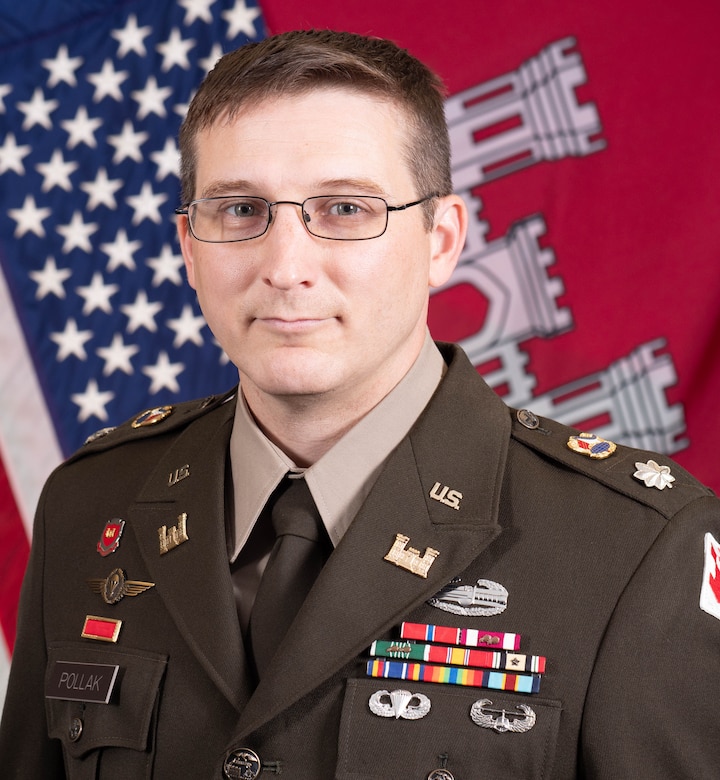 Man in US Army uniform poses for photograph in front of American flag.