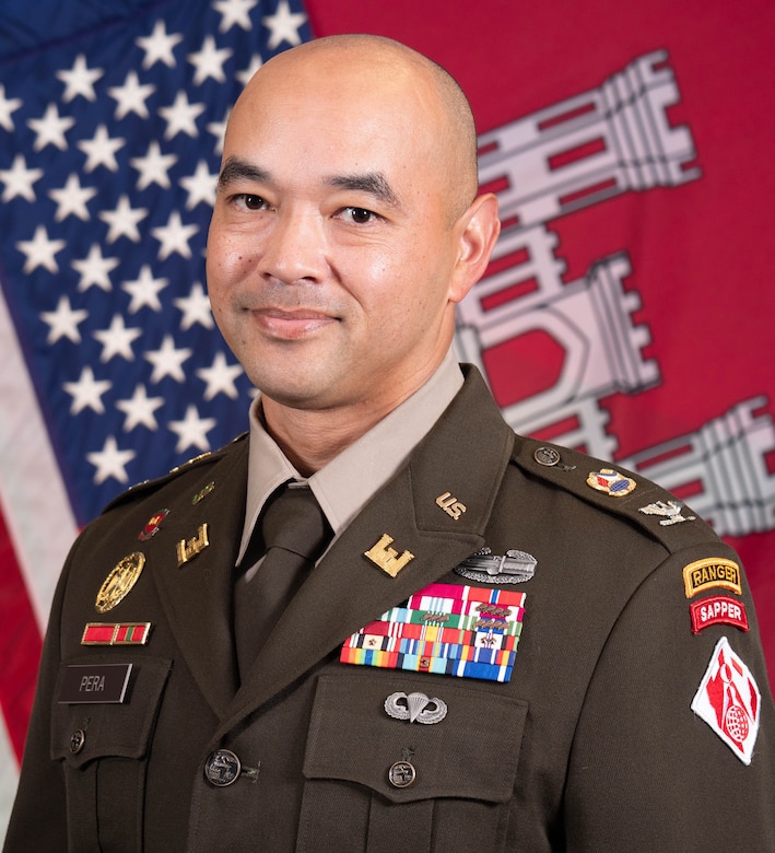 Man in US Army uniform poses for photo in front of American flag.