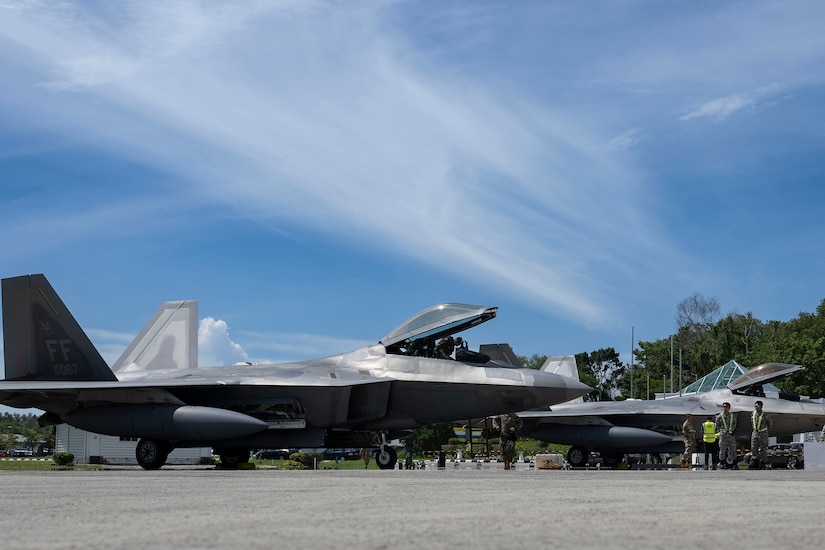 Military aircraft are parked on the tarmac of an airfield during daylight.