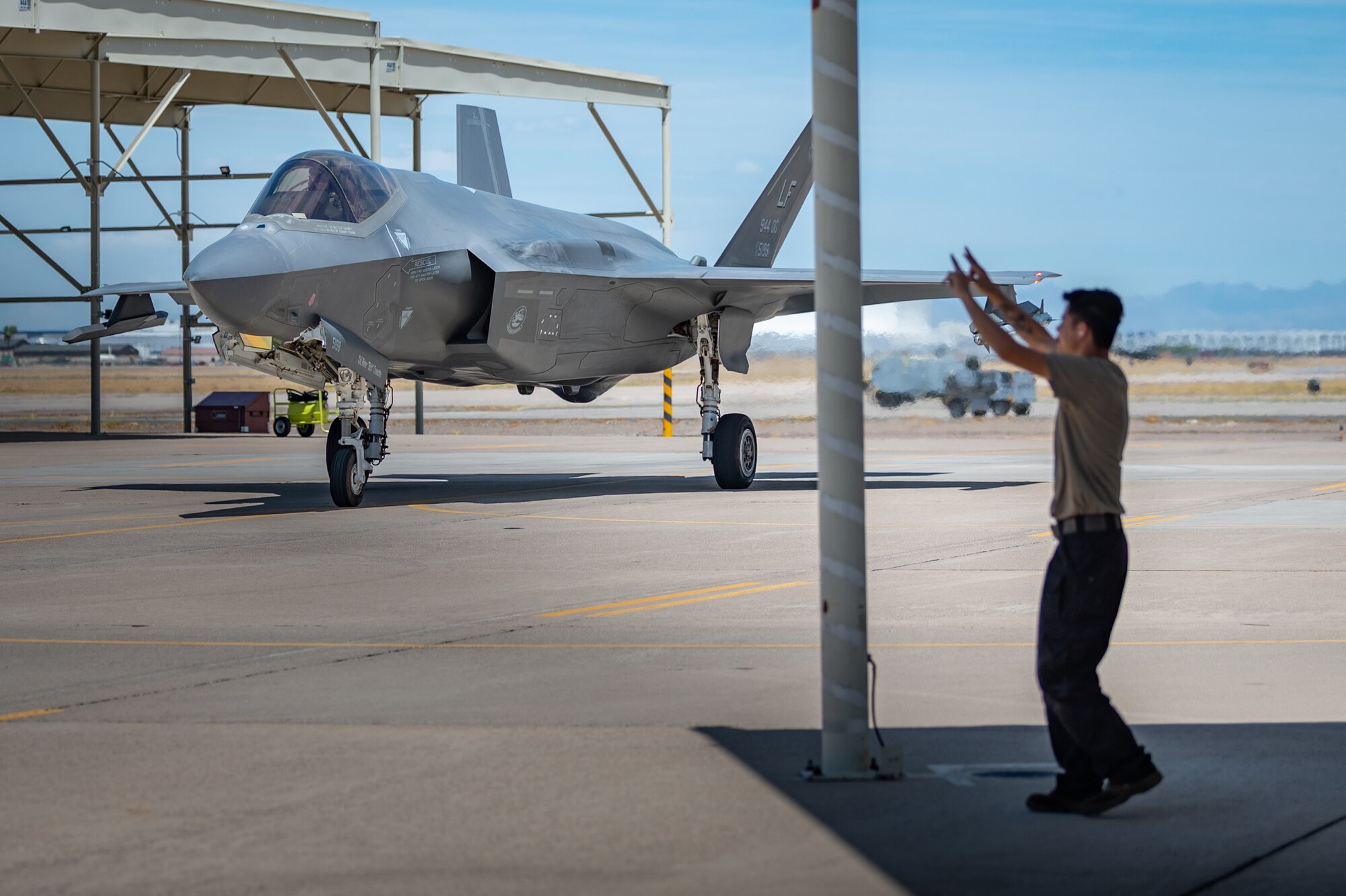 Airman 1st Class Christian Dickinson, an active-duty crew chief with the 63rd Fighter Squadron, marshals Reserve Citizen Airman Lt. Col. Christopher "Lube" Lowe, an F-35 instructor pilot, as he returns from a milestone flight at Luke Air Force Base, Ariz., Aug. 9, 2024. Lowe, who serves as the 56th Operations Group deputy commander, completed his 1,000th flight hour in the F-35 Lightning II, a significant achievement within the 944th Fighter Wing. (U.S. Air Force photo by Tech. Sgt. Tyler J. Bolken)