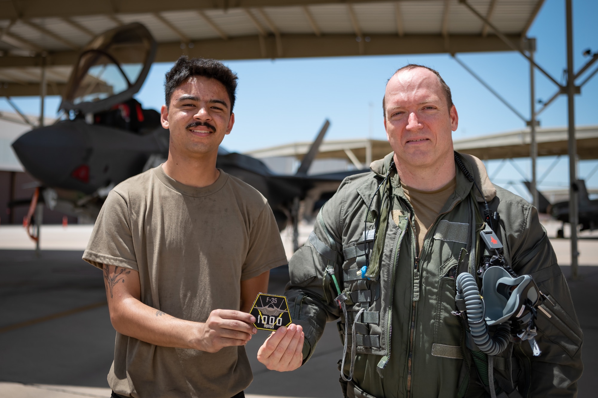 Airman 1st Class Christian Dickinson, an active-duty crew chief with the 63rd Fighter Squadron, and Reserve Citizen Airman Lt. Col. Christopher "Lube" Lowe, F-35 instructor pilot and 56th Operations Group deputy commander, proudly hold the 1,000-hour flight patch after Lowe's milestone flight in the F-35 Lightning II at Luke Air Force Base, Ariz., Aug. 9, 2024. The patch symbolizes not only Lowe’s achievement but also the critical support provided by ground crews like Dickinson. (U.S. Air Force photo by Tech. Sgt. Tyler J. Bolken)