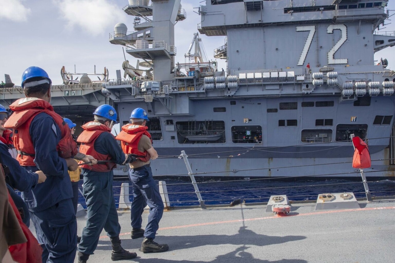 Sailors are on deck of one ship as it sails alongside another ship.