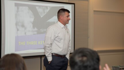 Chaplain Hunter standing in front of room talking in front of projector screen.