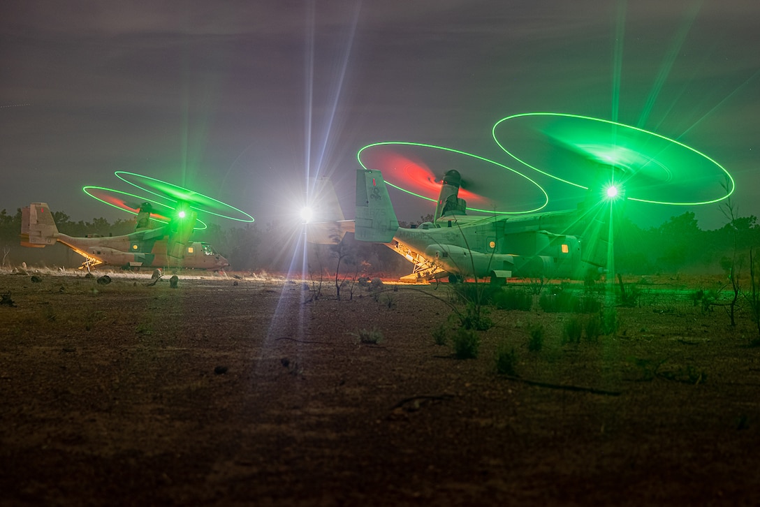 Marine helicopters with green, white and red lights are parked in a desert area at night.