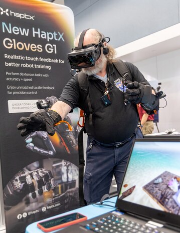 Kristopher Stafford, NNPI control officer, Code 1121, Navy Nuclear Propulsion Control Office, tests a pair of New Haptx Airpack Gloves while using a Virtual Reality headset July 31, 2024, during the annual Puget Sound Naval Shipyard & Intermediate Maintenance Facility Technology Showcase at the Kitsap Conference Center in downtown Bremerton, Washington. (U.S Navy Photo by Wendy Hallmark)