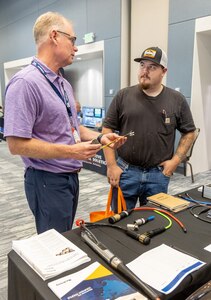 Morgan Myhre, right, electrician/heavy mobile equipment mechanic, Code 730, Crane Maintenance, talks with Don Bryan, of Macartney Underwater Technology, July 31, 2024, during the annual PSNS & IMF Technology Showcase at the Kitsap Conference Center in downtown Bremerton, Washington. (U.S Navy Photo by Wendy Hallmark)