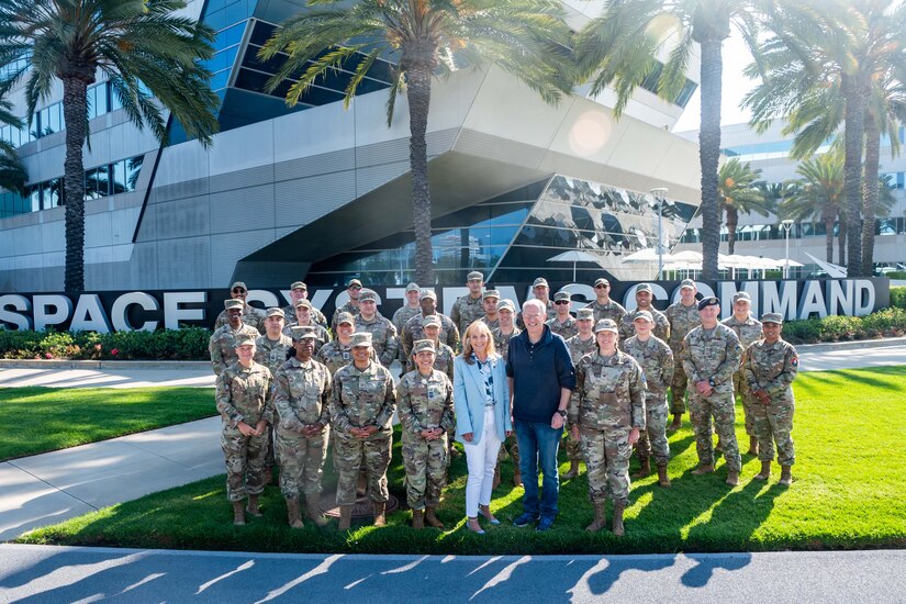 Civilians and service members stand in a group in front of a building and pose for a photo.