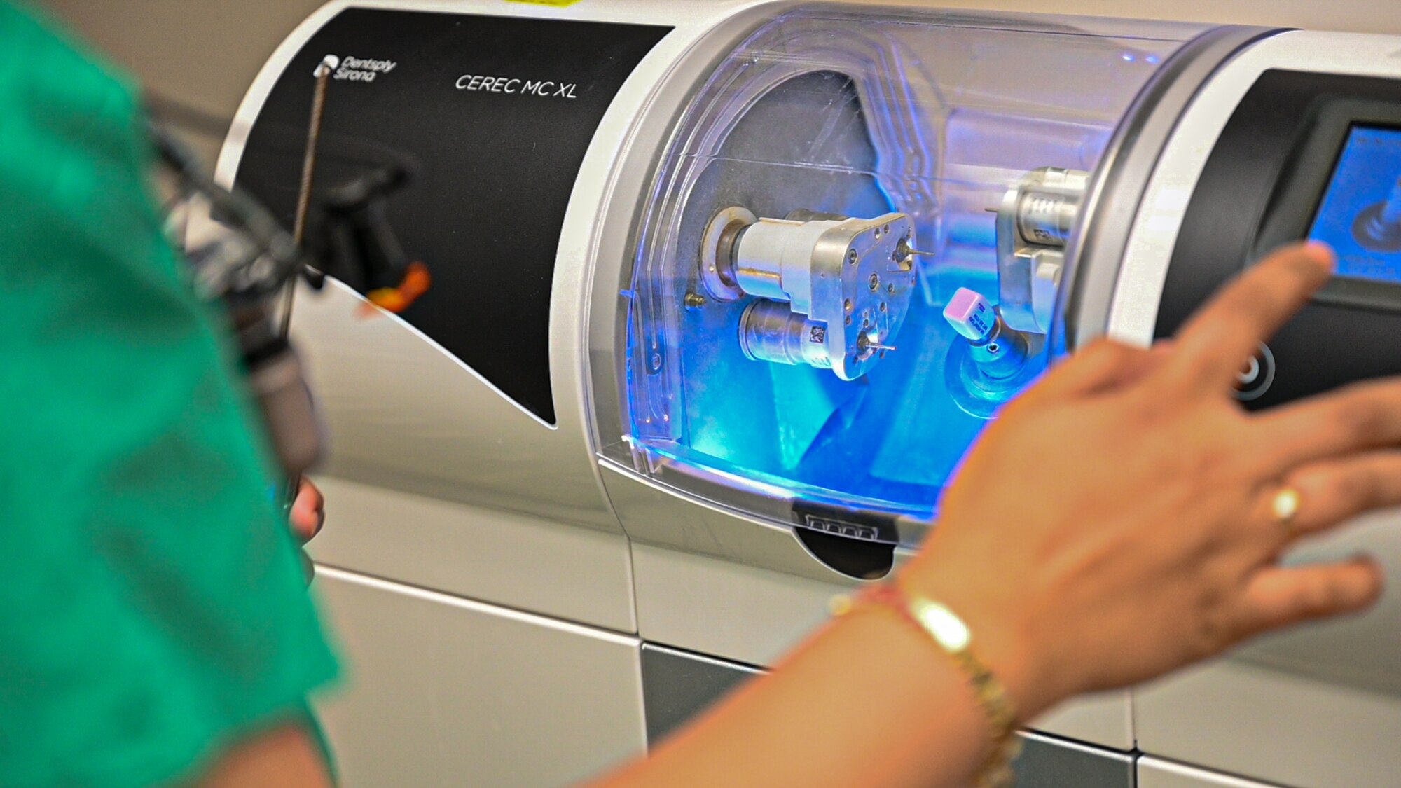 Photo of an Airman pushing a button on a machine to create a crown out of ceramic material.