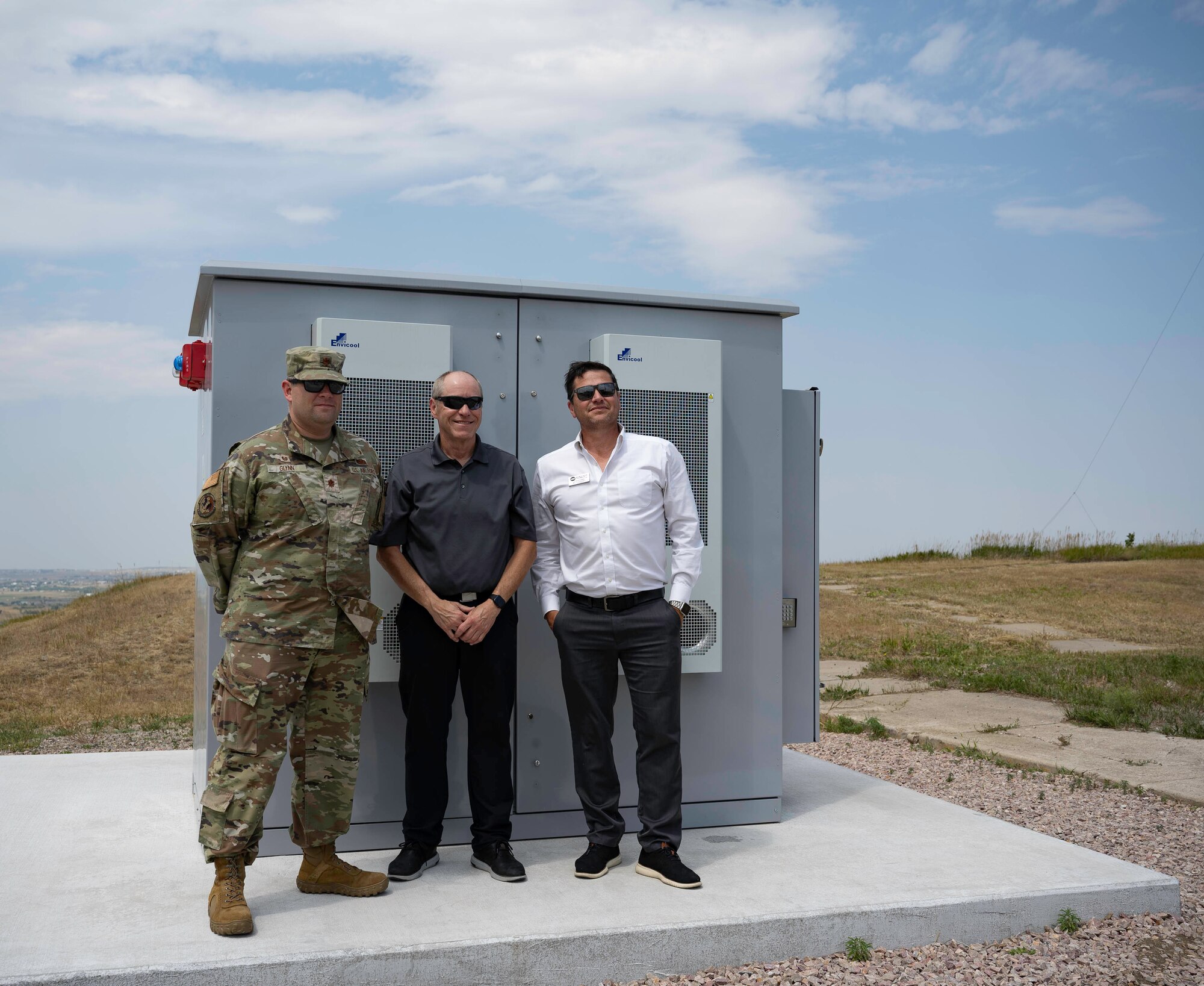 U.S. Air Force Maj. Michael Glynn, 28th Logistics Readiness Squadron commander (left), Richard Johnson, CEO and manager, West River Electric Association (center), and Robert Raker, Manager of Public Relations, West River Electric (right), pose for a photo in front of a Battery Energy Storage System in Box Elder, S.D., 22 July, 2024. Ellsworth Air Force Base worked with West River Electric Association (WREA), SAFT/GoElectric, the National Rural Electric Cooperative Association (NRECA), Pacific Northwest National Lab, and Sandia National Laboratories using a Department of Energy (DOE) grant to action the project. (U.S. Air Force photo by Senior Airman Josephine Pepin)