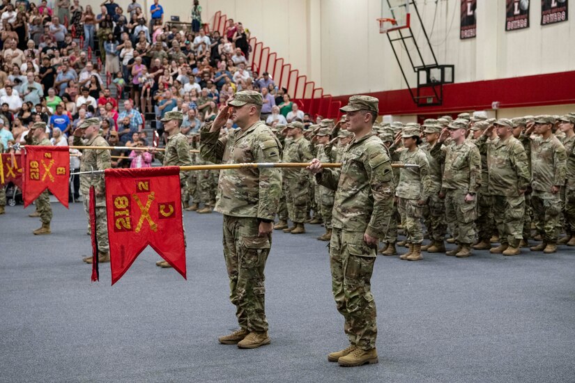 Soldiers salute during a ceremony while other soldiers hold flags.