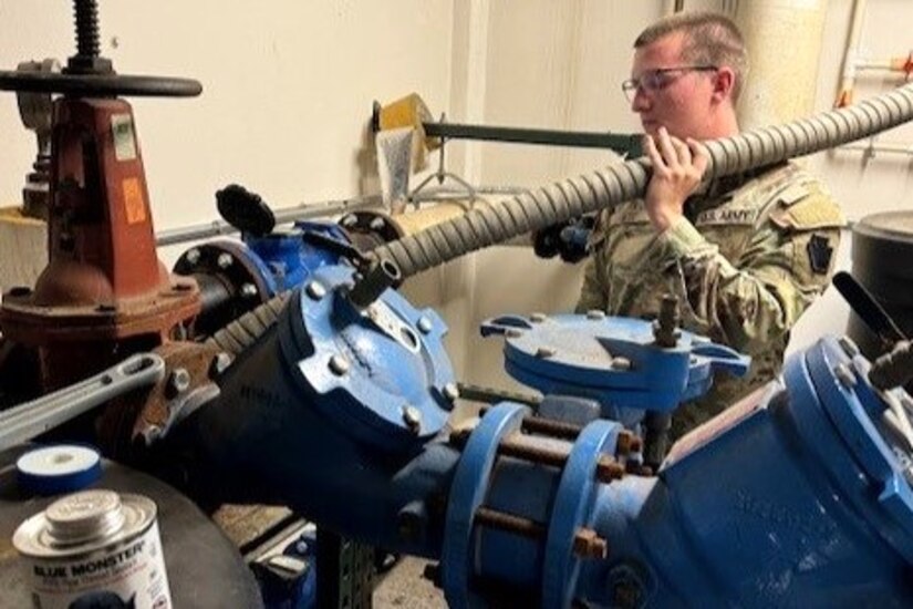 Spc. Andrew Getz, assigned to the 628th Aviation Support Battalion, 28th Expeditionary Combat Aviation Brigade, 28th Infantry Division, hooks up a hose from an M105 Load Handling System Compatible Water Tank Rack, also known as a HIPPO bulk water distribution system, to the main water line at Penn State Health Holy Spirit Medical Center to build pressure and transfer potable water during an emergency response mission at Camp Hill, Pennsylvania, Aug. 10, 2024. The mission was to provide potable water after an emergency water advisory affected nearly 42000 customers in that part of the commonwealth. Getz and other Soldiers with the 628th ASB responded to a call from the Pennsylvania Emergency Management Agency for the Pennsylvania National Guard to assist. (Courtesy Photo)