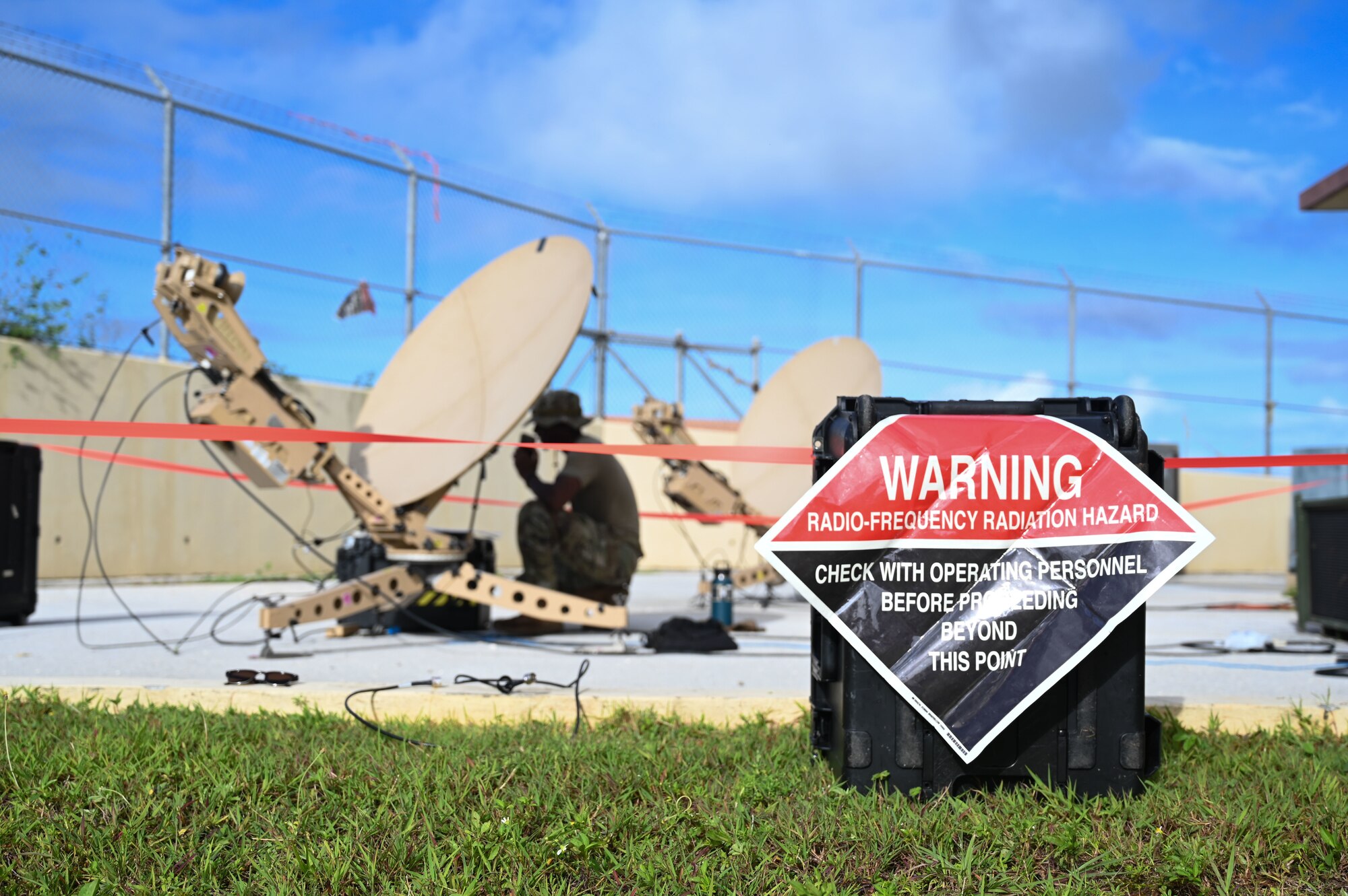 A black and red Hazard Warning sign marks the area where the tan satellite communication dishes were erected.