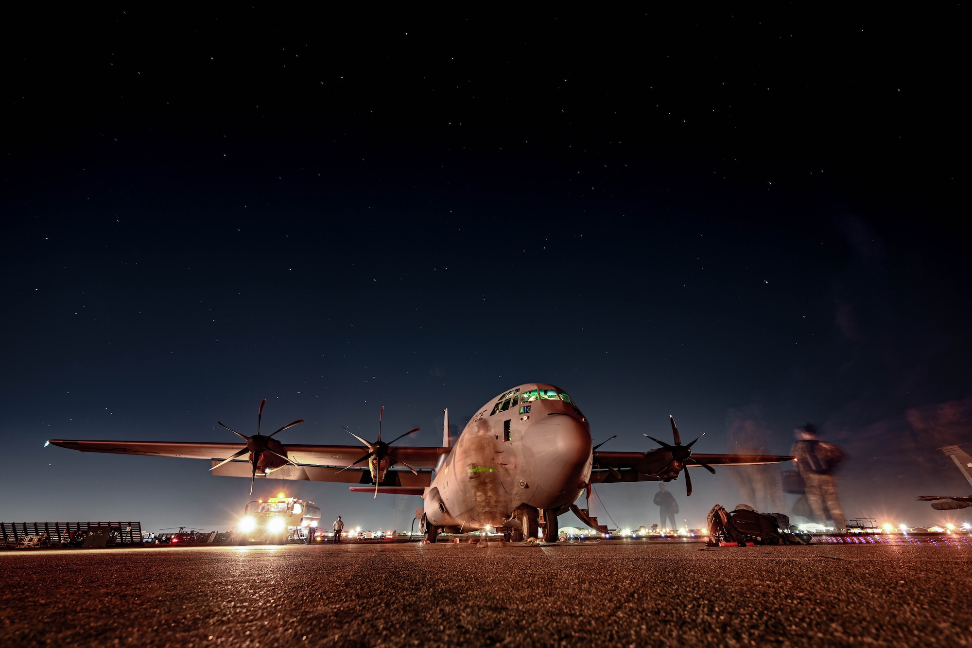 A C-130J Super Hercules sits on the flightline under a star-lit night sky.
