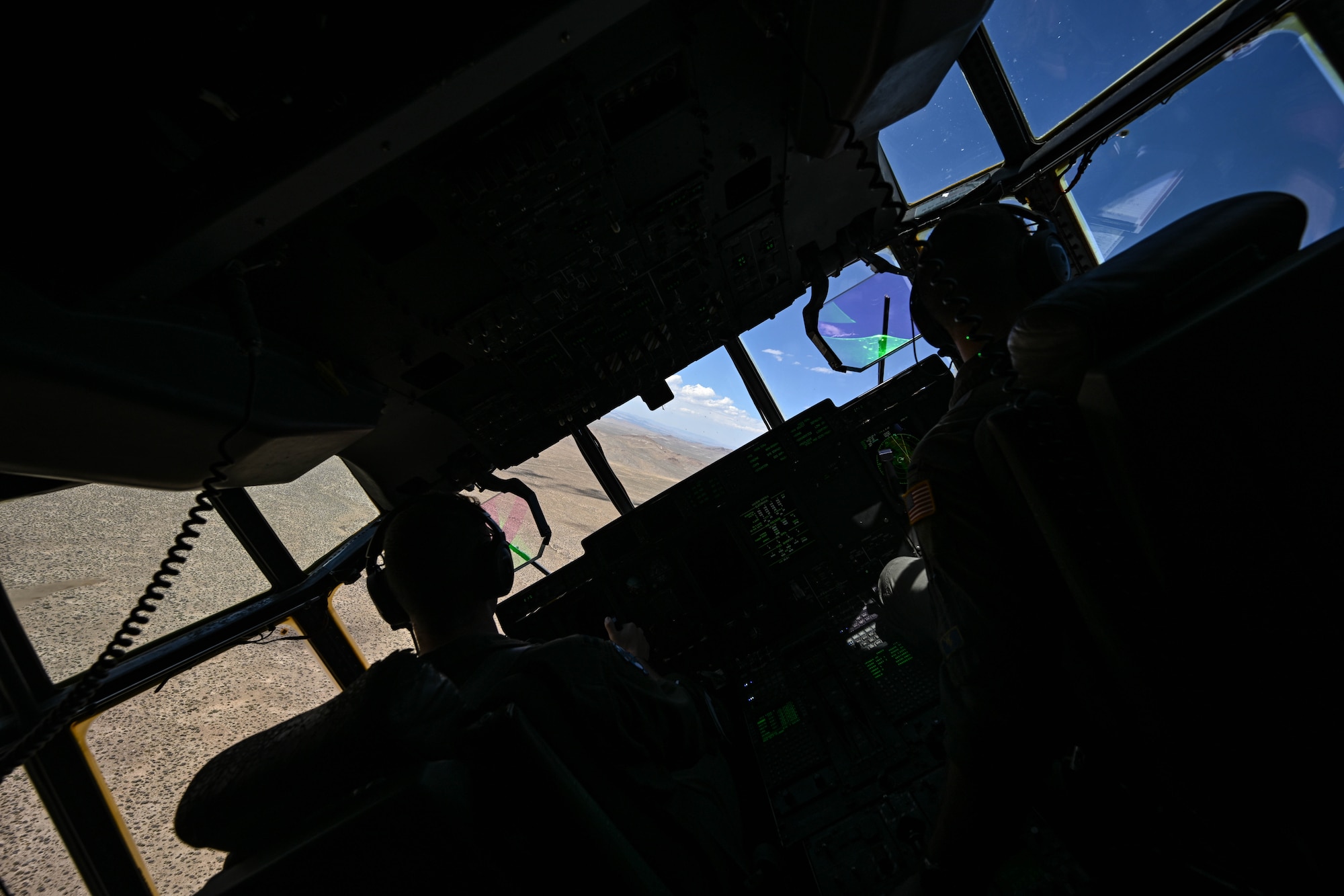 From the inside of a C-130J Super Hercules aircraft, the camera captures a steep banking turn over desert terrain.