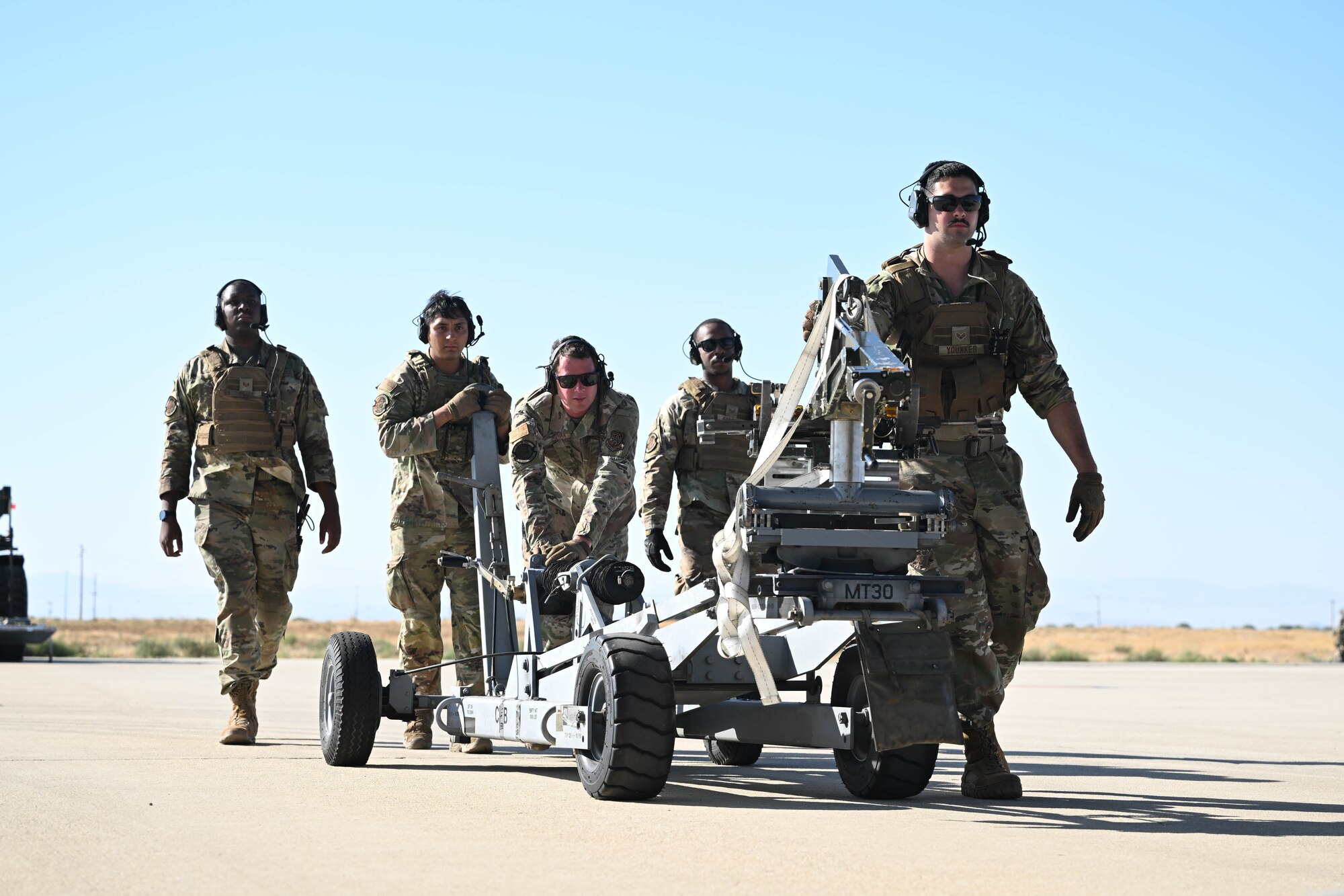 Men in uniform move cargo loading equipment across the flightline during the day.
