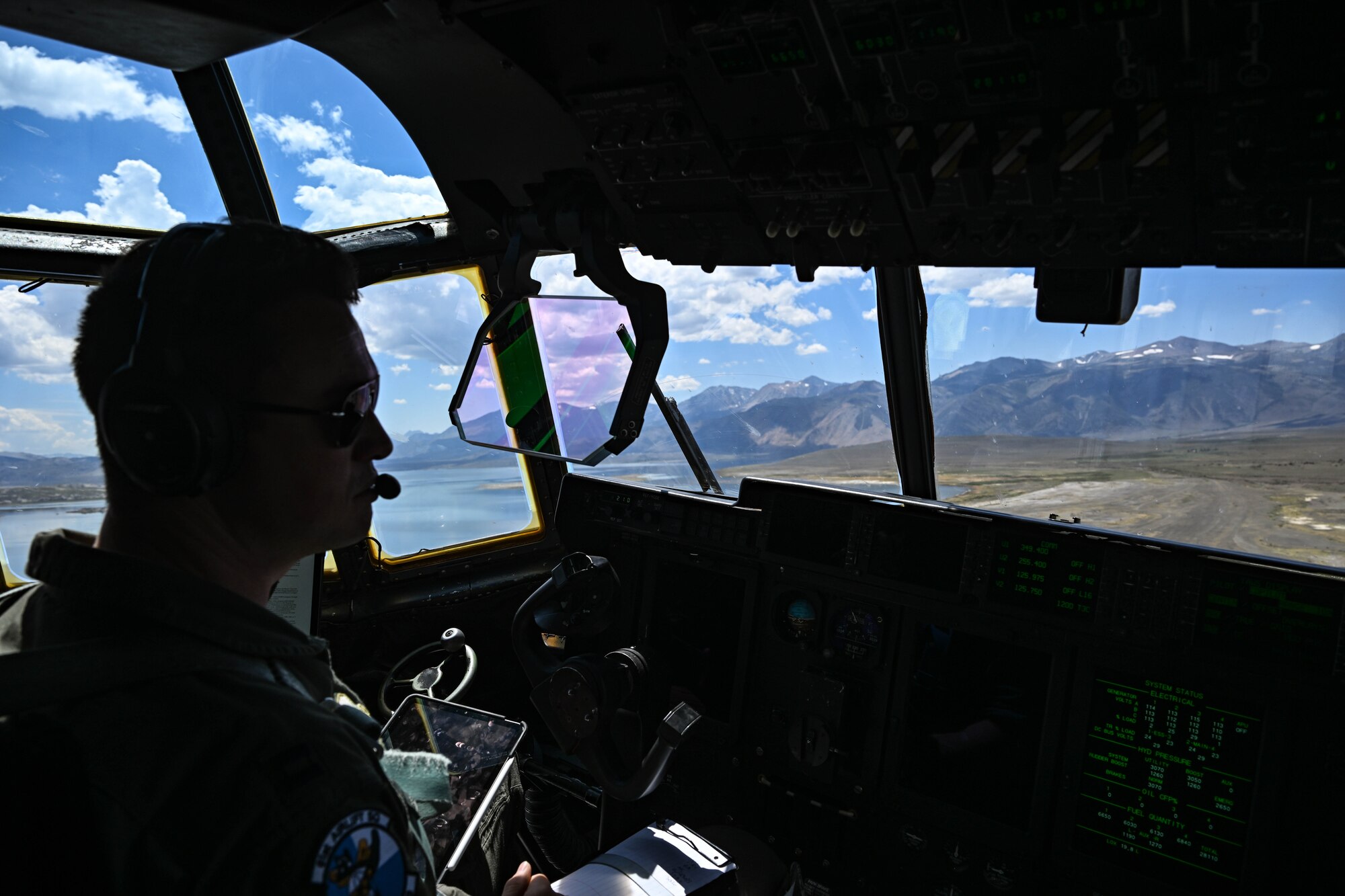 A C-130J Super Hercules aircraft pilot sits in the cockpit flying low over desert terrain.