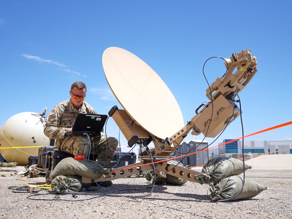 Man in uniform working on laptop connected to small satellite dish