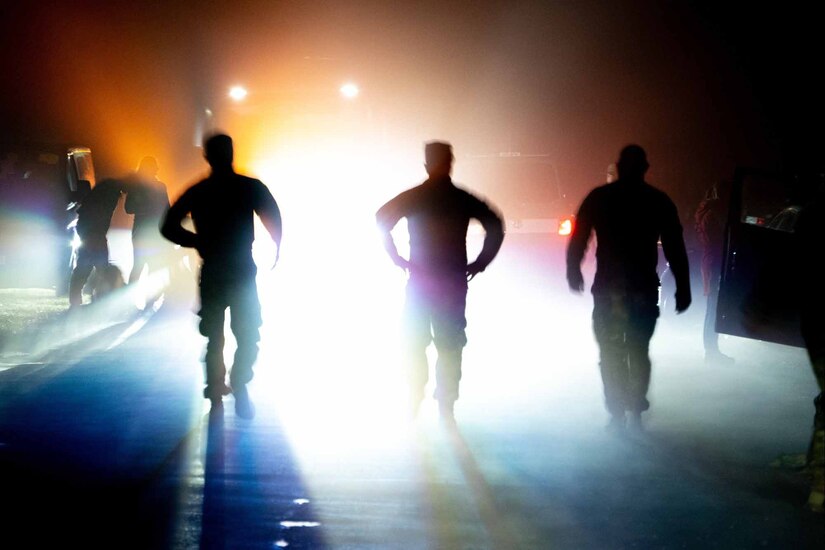 Three soldiers stand silhouetted by backlights.