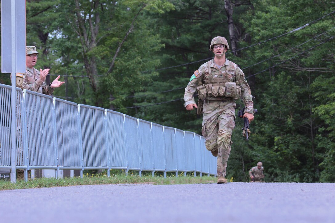 Spc. Tevin Kenton, representing the Wisconsin Army National Guard, crosses the biathlon finish line Aug. 6 as Command Sgt. Maj. Duane Weyer, the state command sergeant major for the Wisconsin Army National Guard, cheers Kenton on during the 2024 Army National Guard Best Warrior Competition at Ethan Allen Firing Range, Vt. Kenton is an infantryman assigned to Troop C, 1st Squadron, 105th Cavalry Regiment. U.S. Army National Guard photo by Sgt. Olivia Gum