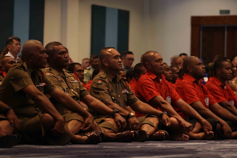 Several males sit on a floor wearing military and ceremonial attire.