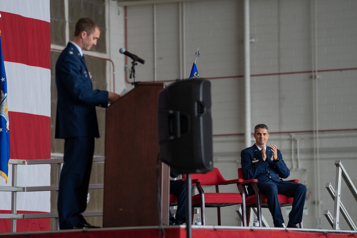 A seated Airman claps as another finishes a speech