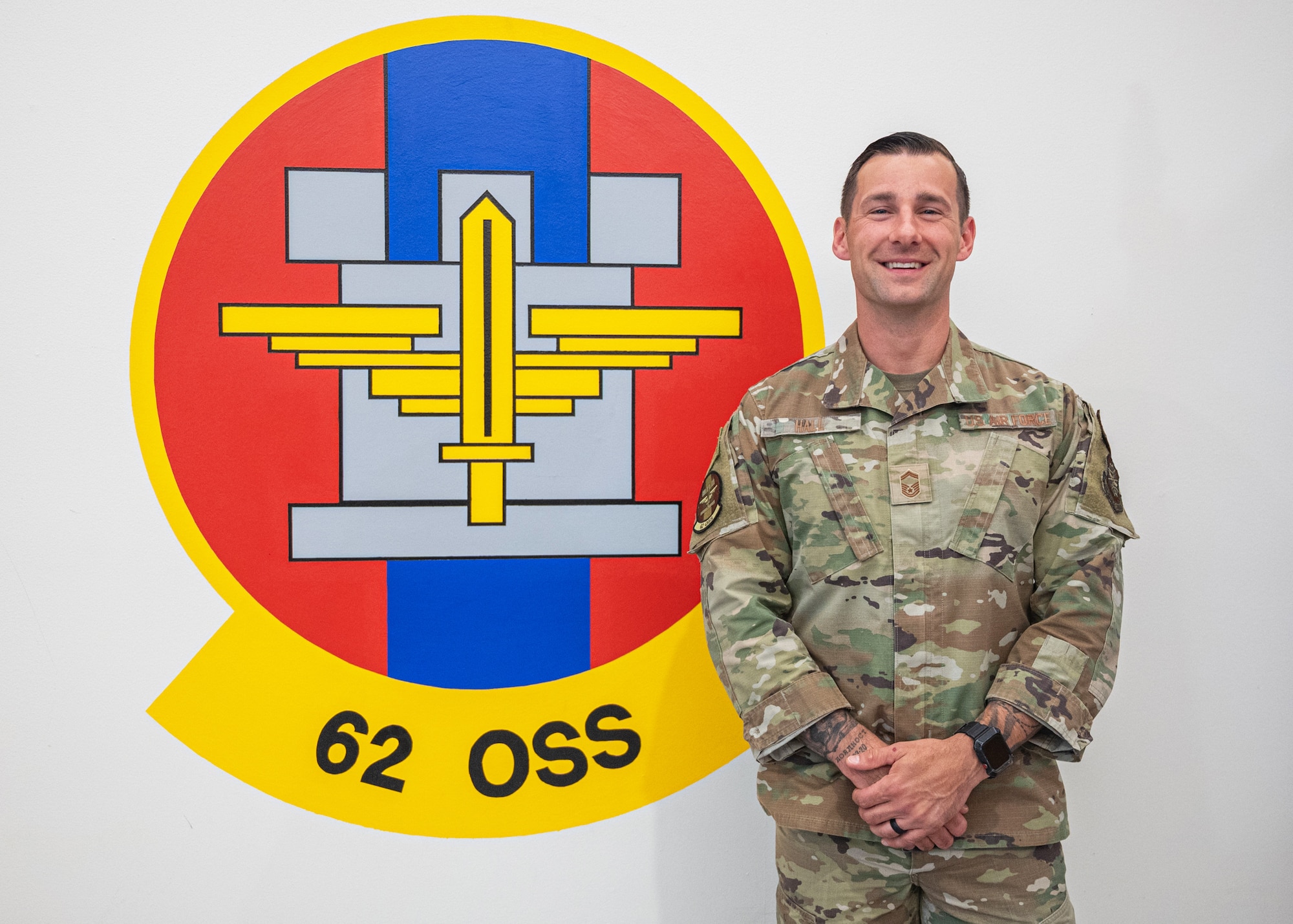 U.S. Air Force Senior Master Sgt. Joshua Hall, 62d Operations Support Squadron aircrew flight equipment superintendent, stands in front of the 62d OSS logo at Joint Base Lewis-McChord, Washington, Aug. 13, 2024.