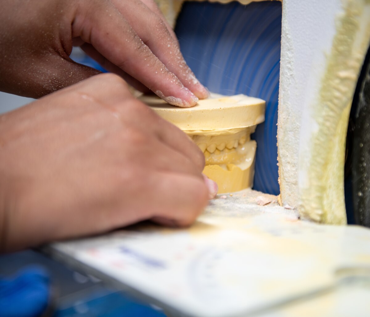 An individual shaping a dental cast using a grinder.