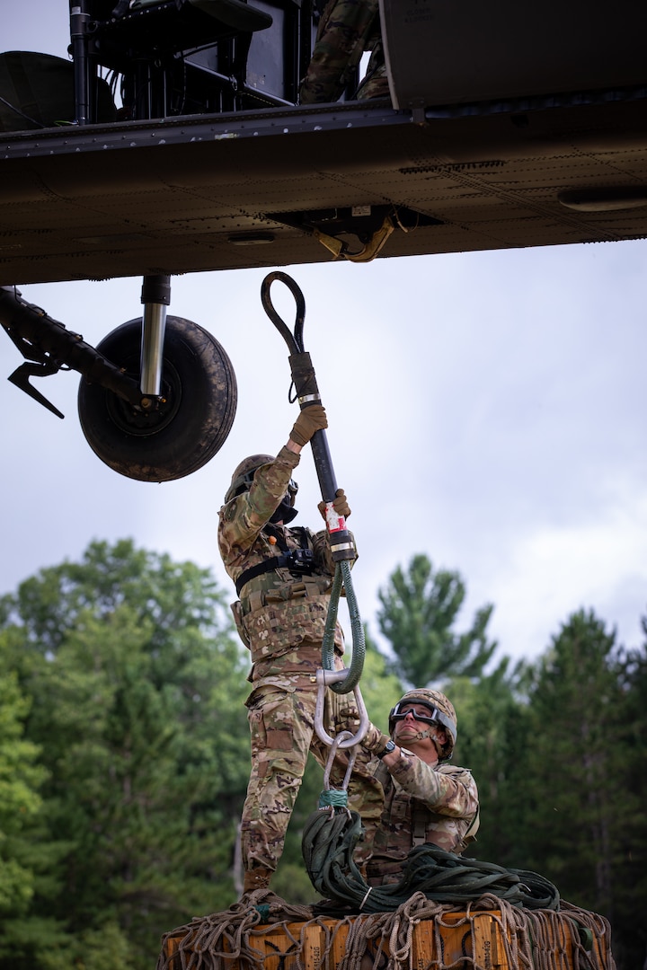 Oklahoma Army National Guard Spc. Michael Champion, a combat medic assigned to headquarters battery, 1st Battalion, 160th Field Artillery Regiment, 45th Infantry Brigade Combat Team, hooks a cargo load of ammo to a UH-60 Black Hawk during emergency airlift resupply training at Exercise Northern Strike 2024, Camp Grayling, Michigan, Aug. 11, 2024.