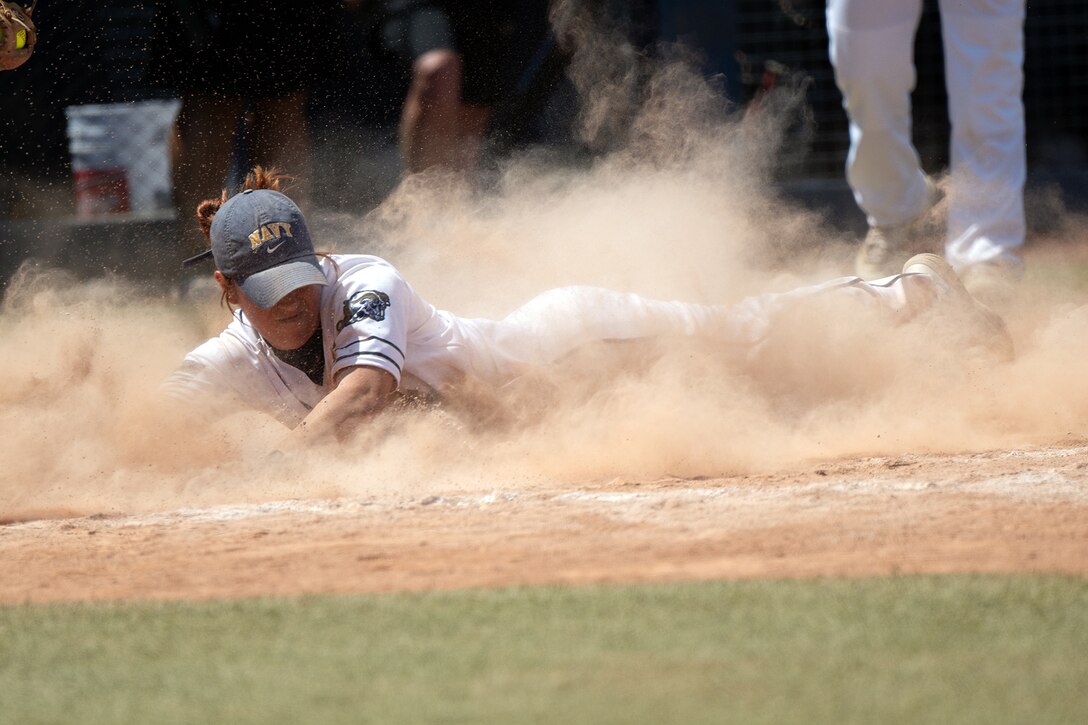 A softball player slides into home plate creating a large cloud of dust.