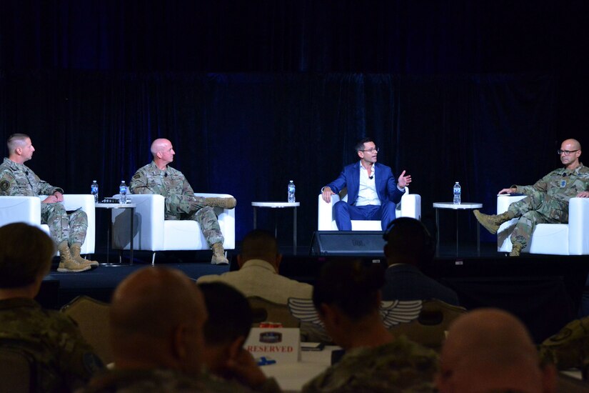 Four people sit in chairs on a stage and talk.