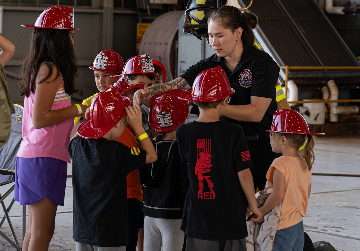 Andrea Schanze, 788th Civil Engineer Squadron fire inspector, places helmets on children during  Kids Understanding Deployment Operations event at Wright-Patterson Air Force Base, Ohio, Aug.9, 2024.