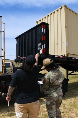 A woman points at a truck while an Air Force reservist dressed in camouflage takes notes in a notebook