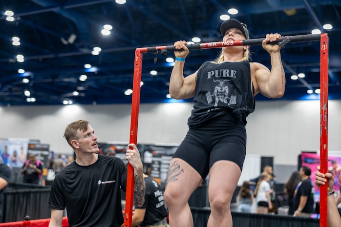U.S. Marine Corps Sgt. Mathew Miller, left, a recruiter with Recruiting Sub Station Baybrook,  Recruiting Station Houston, stabilizes a pull-up bar for an attendee during the American Fitness Expo at the George R. Brown Convention Center in Houston, Texas, Aug. 3, 2024. Marines with RS Houston held a recruiting booth alongside fitness influencers, health vendors; and professional athletes to challenge attendees and vendors alike in a pull-up bar challenge. (U.S. Marine Corps photo by Sgt. Ryan H. Pulliam)