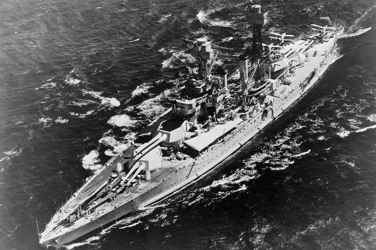 An aerial view  of a battleship steaming through the ocean.