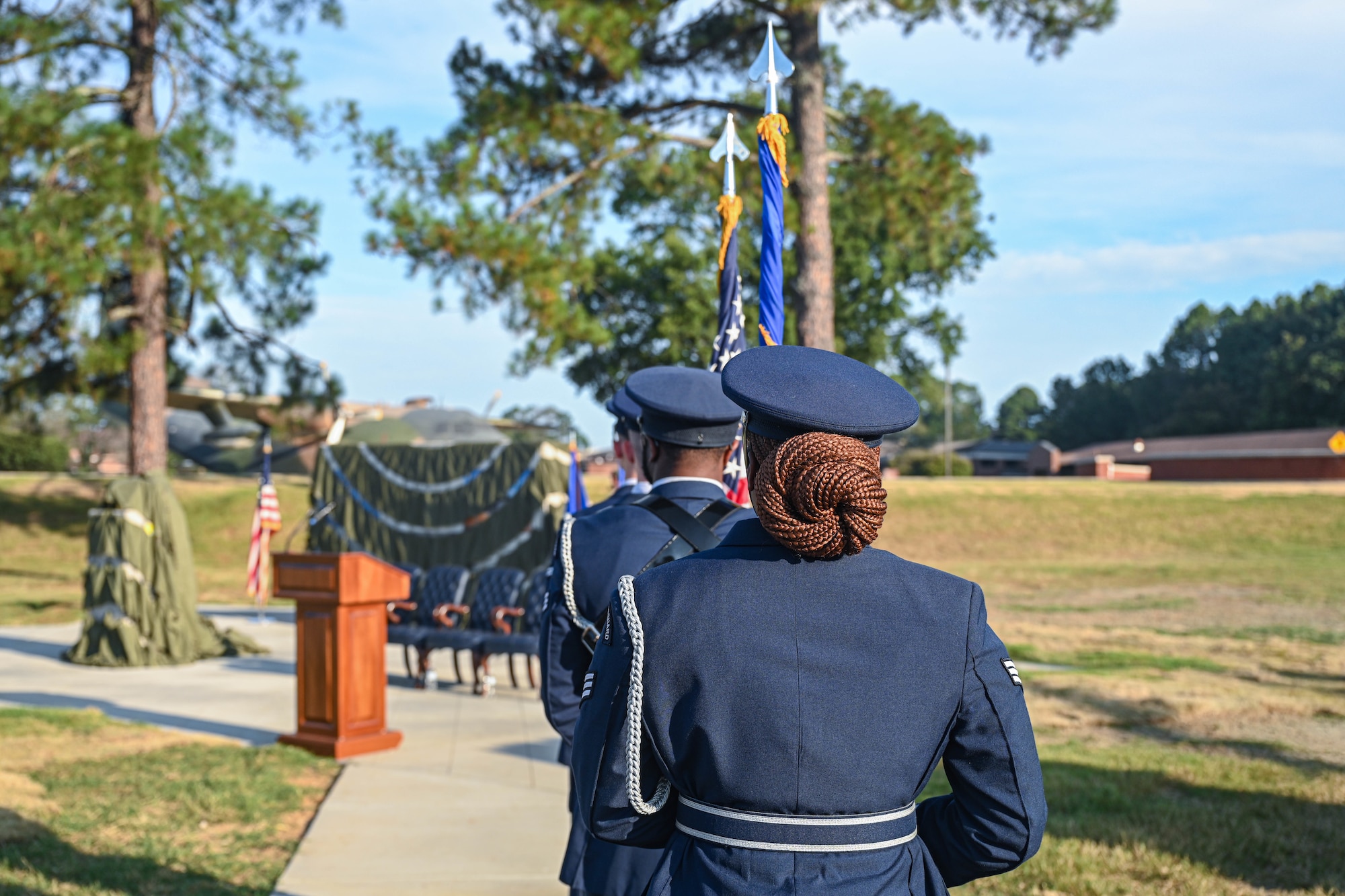 A group of uniformed personnel walk towards the front of a ceremony in single file.