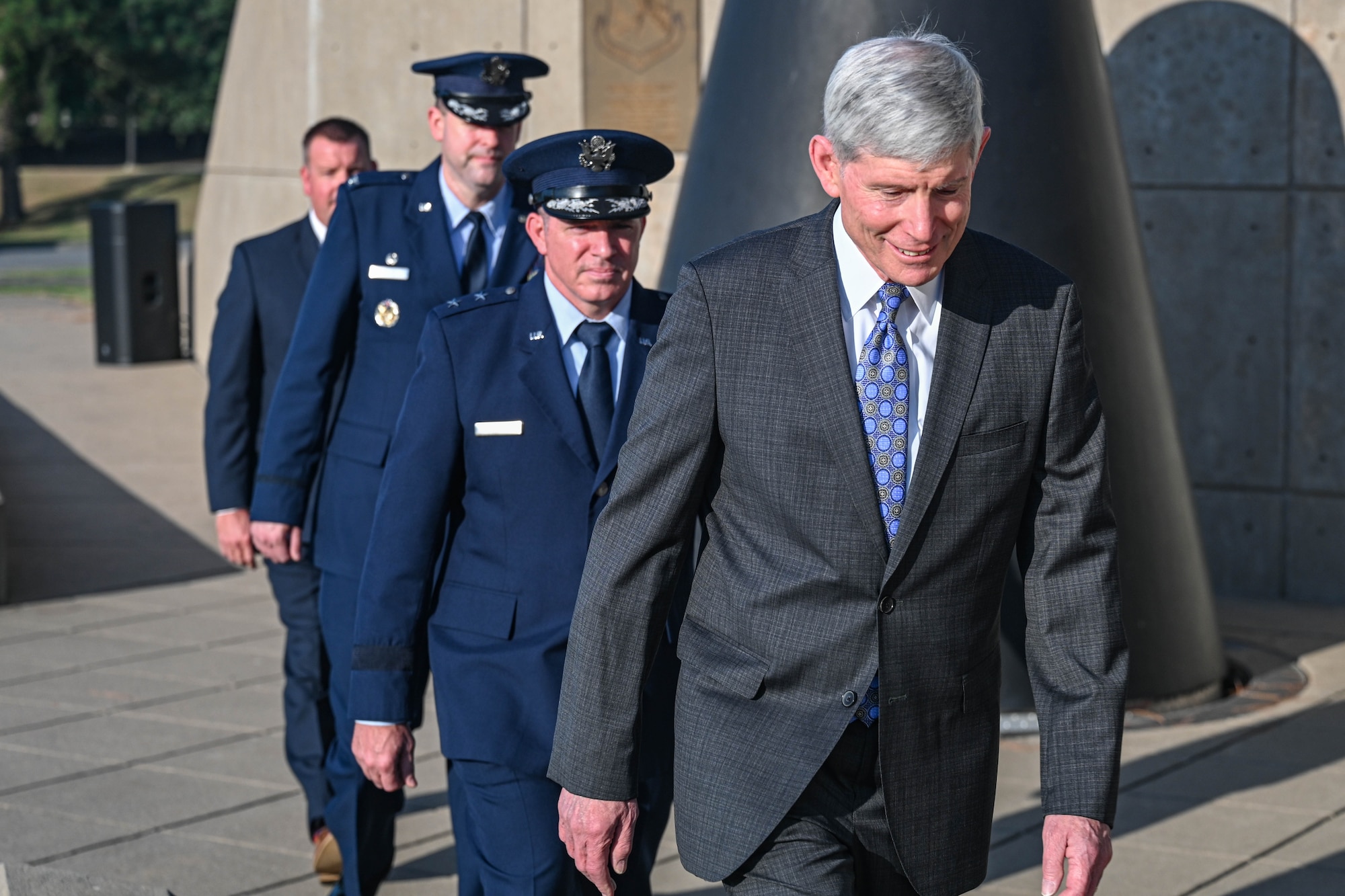 Men in a single-file line walk towards a dedication ceremony.