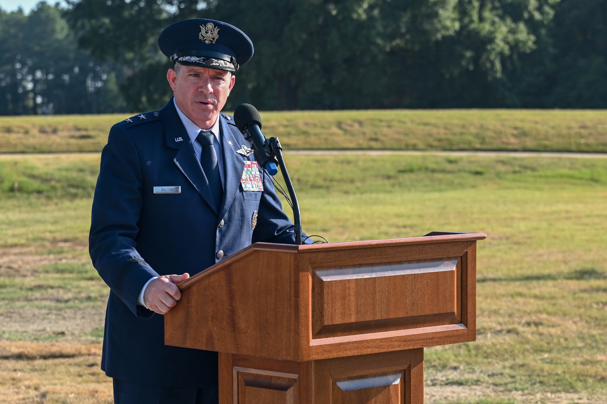 A man in uniform stands behind a podium and addresses a crowd at a dedication ceremony.