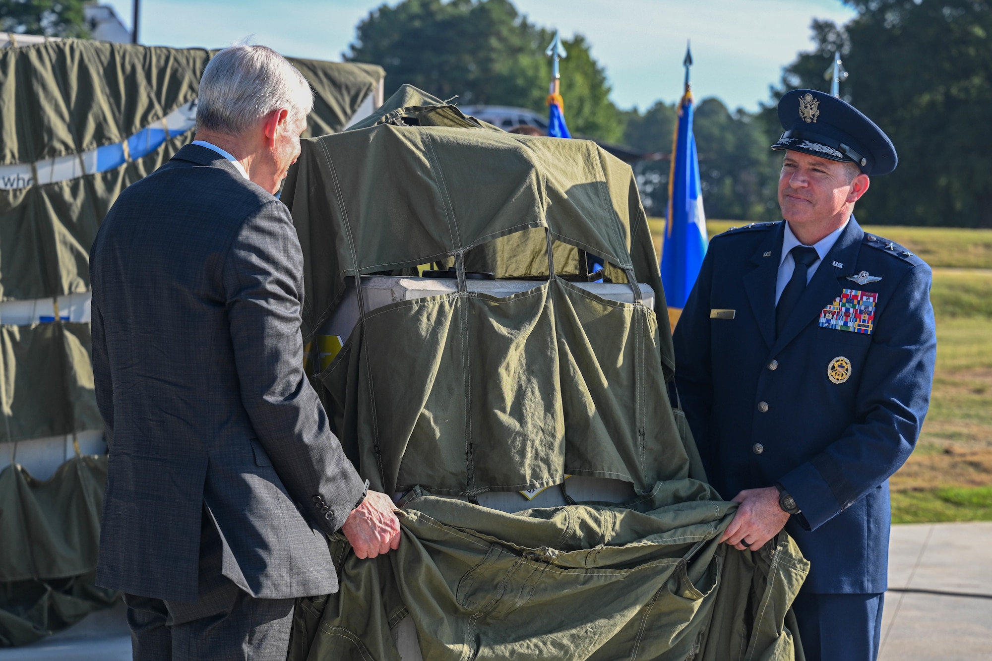 Two men hold a tarp which is covering a monument set to be unveiled.