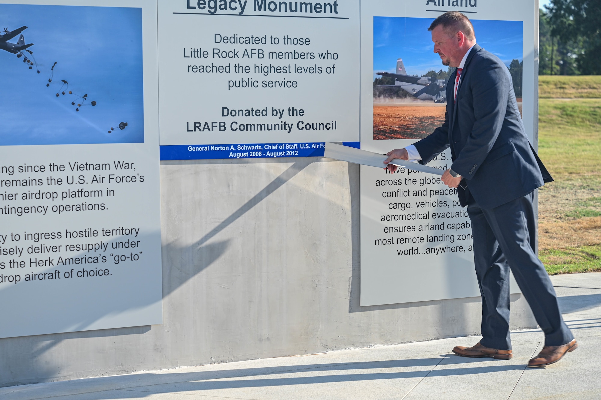 A man peels tape off of a nameplate on a monument at a ceremony.