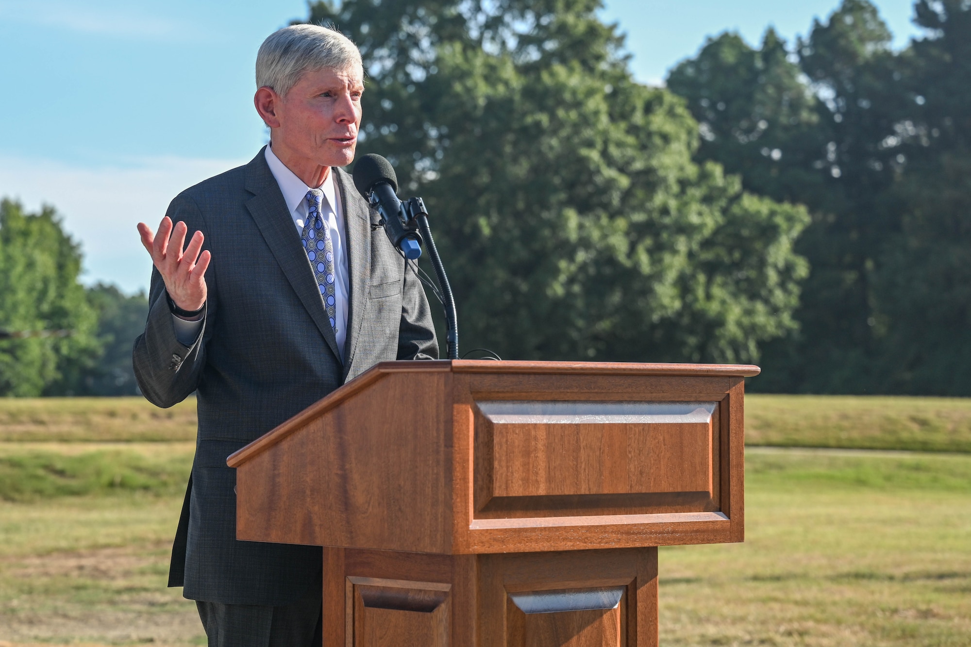 A man behind a podium speaks to a crowd at a dedication ceremony.
