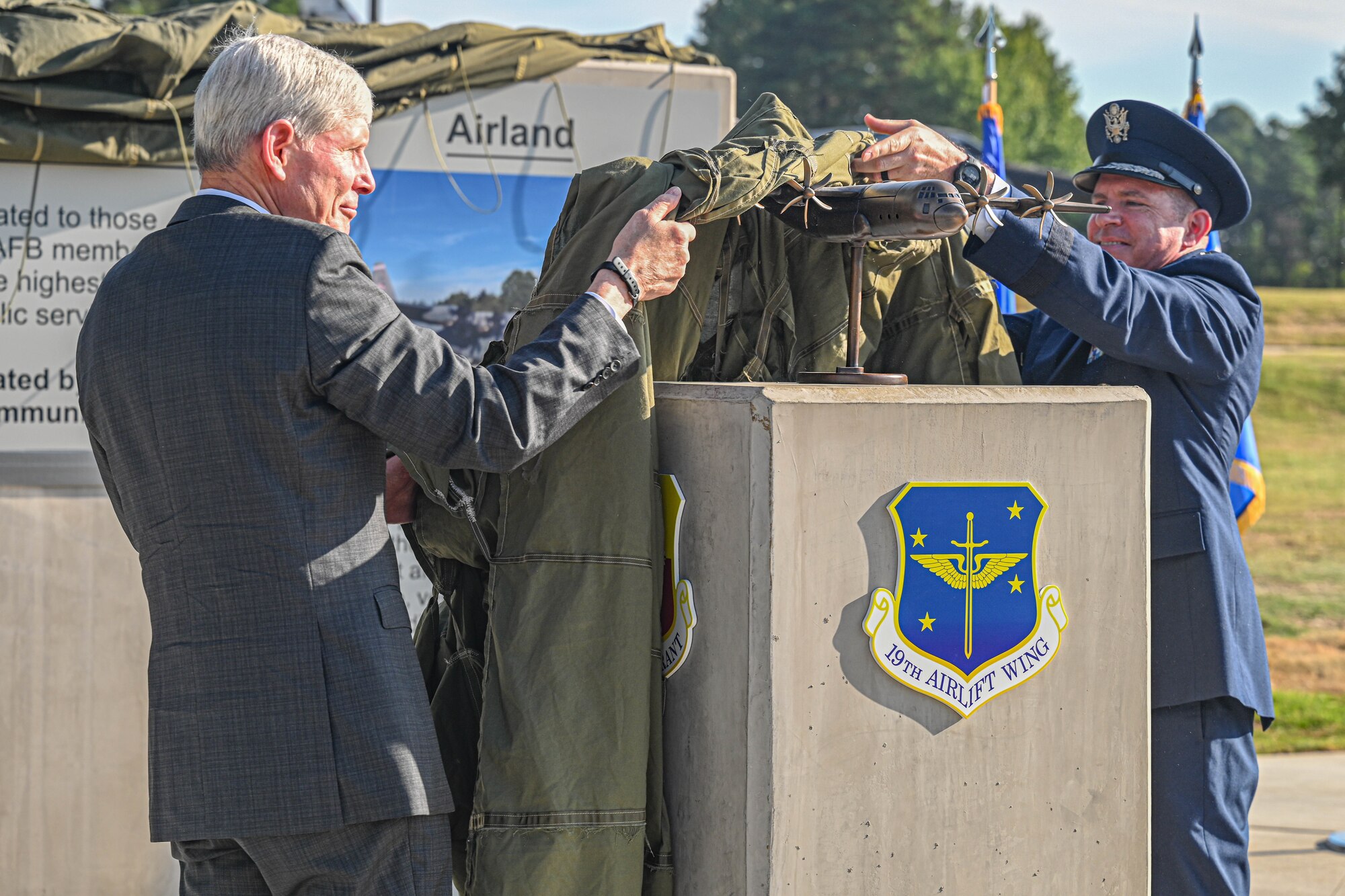 Two men unveil a bronze statue at a dedication ceremony.