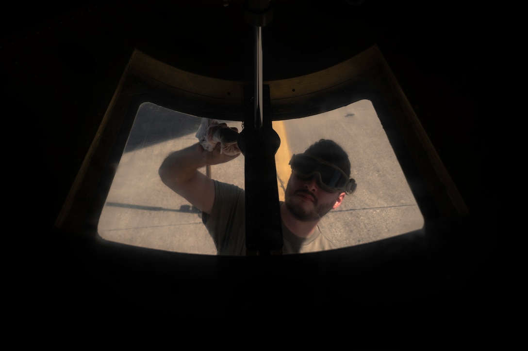 An airman, viewed from above, reaches up to clean an aircraft window framed by darkness.